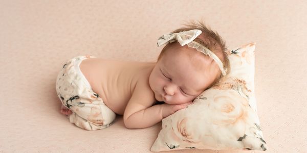 Peaceful newborn baby sleeping on a floral pillow with matching headband and pants.
