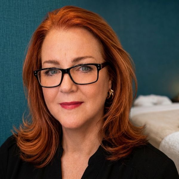 Confident woman with red hair and glasses in a cozy indoor setting.