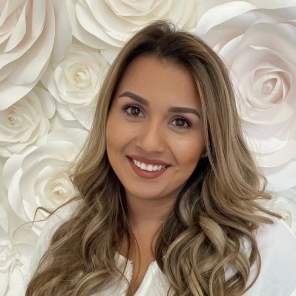 A smiling woman with long wavy hair in front of a white floral background.