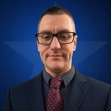 Man in glasses and suit smiling in front of blue star background.