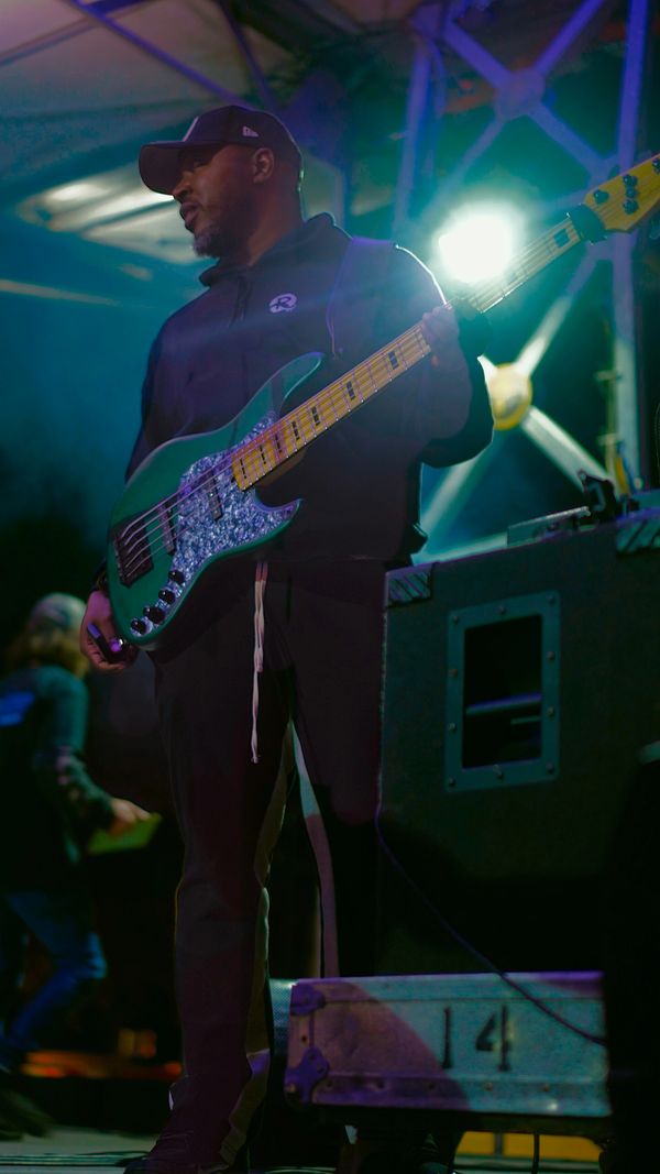 Musician playing bass guitar on stage under colorful lights.