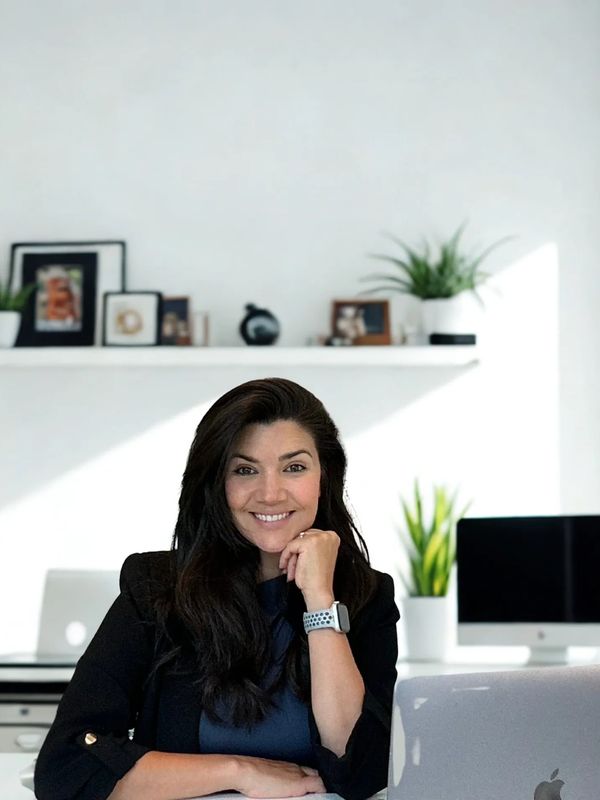 Smiling woman sitting at a desk with a laptop in a modern, bright office.