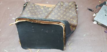 A worn Louis Vuitton bag with detached bottom on a workbench.