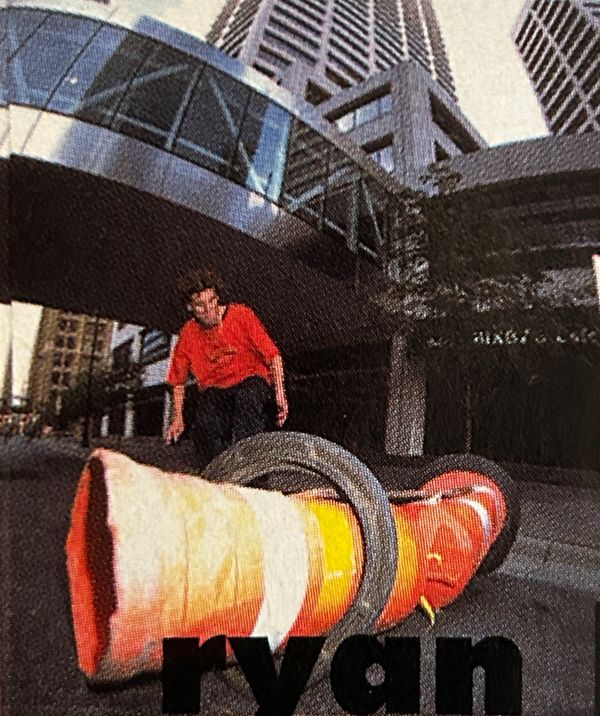 Skateboarder performing a trick over a large traffic cone in the city.