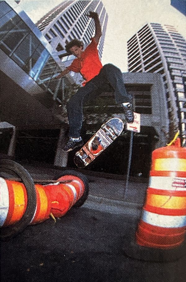 Skateboarder performs a trick jumping over orange traffic cones in an urban setting.