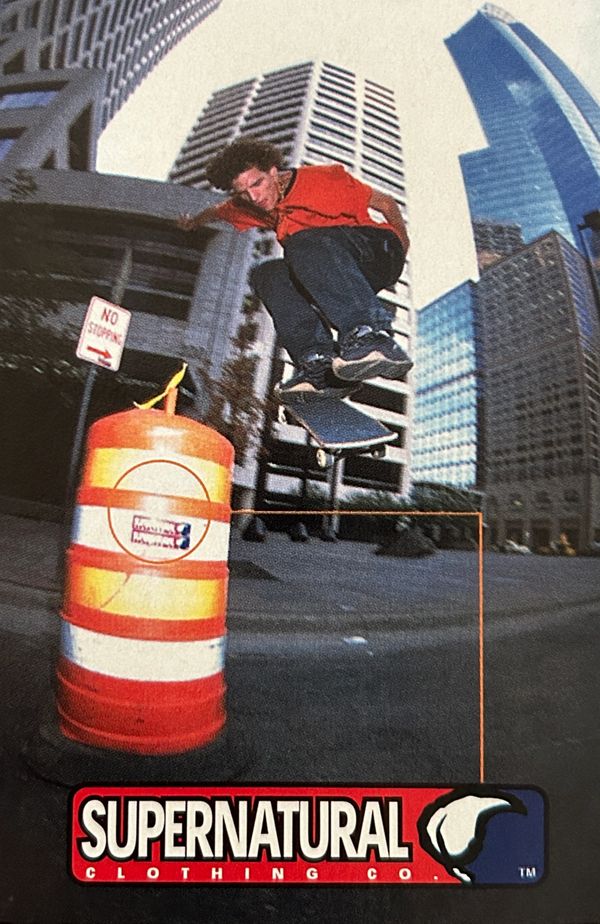 Skateboarder performs a trick mid-air in an urban setting with skyscrapers.