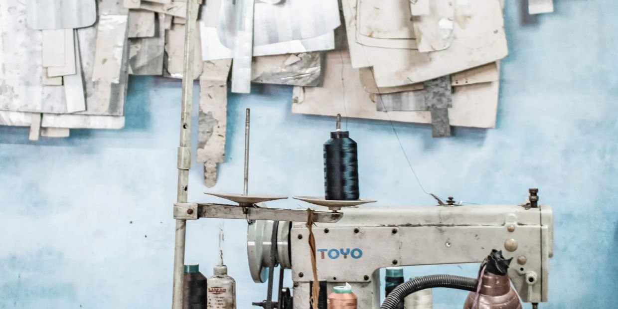 Old sewing machine with thread spools and fabric patterns on a blue wall.