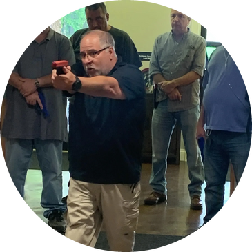 Man aiming a training gun indoors with others observing.