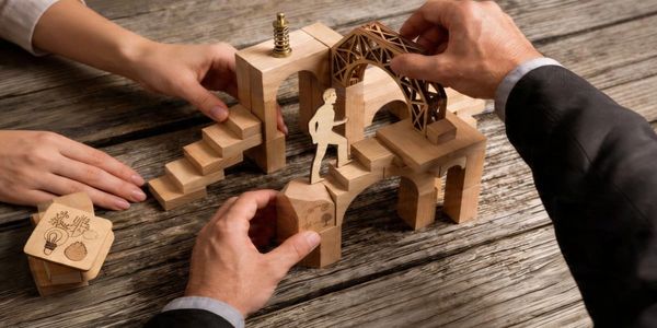 Hands assembling a wooden puzzle with a paper figure climbing stairs.