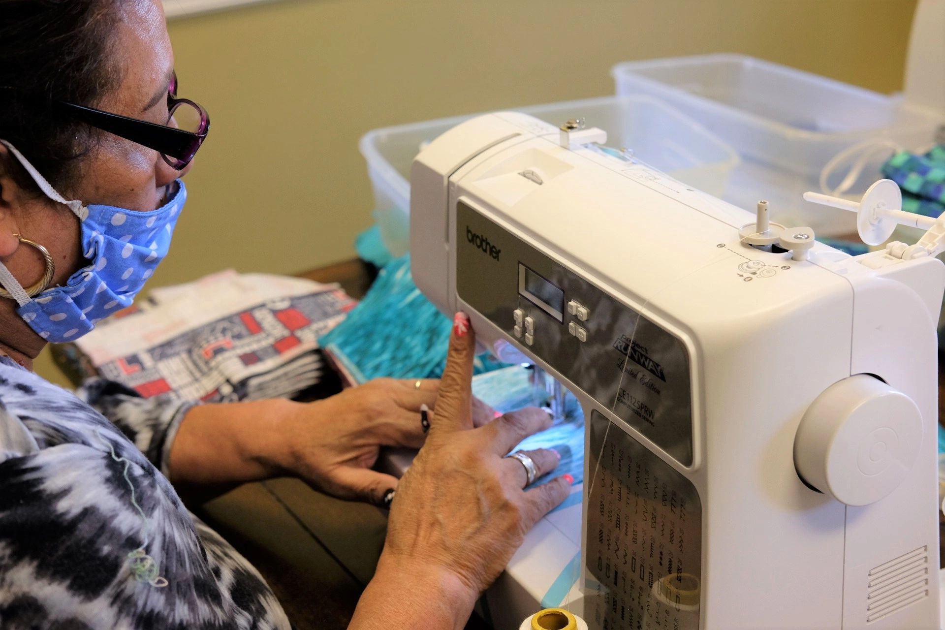 Woman sewing fabric on a machine wearing a face mask.