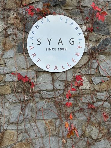 Circular sign for SYAG Art Gallery on a stone wall with climbing red ivy.