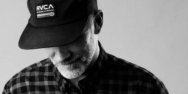 Black and white portrait of a man wearing a cap and checkered shirt.