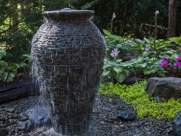 Stack-slate urn with flowing water and plants in the background