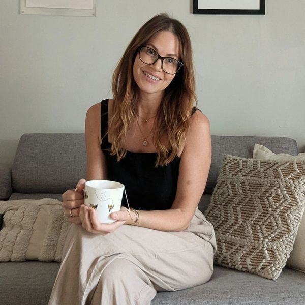 Woman with glasses sitting on a couch holding a mug and smiling.