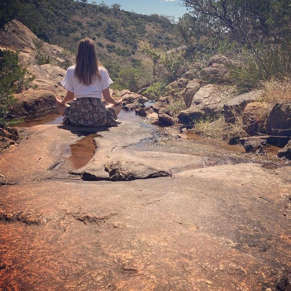 Woman meditating on rocks near a small stream.
