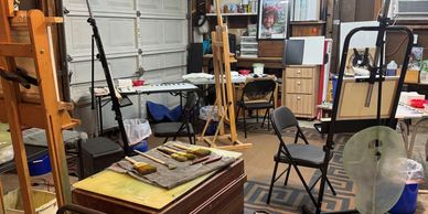 Cozy art studio with easels, brushes, and chairs in a garage space.