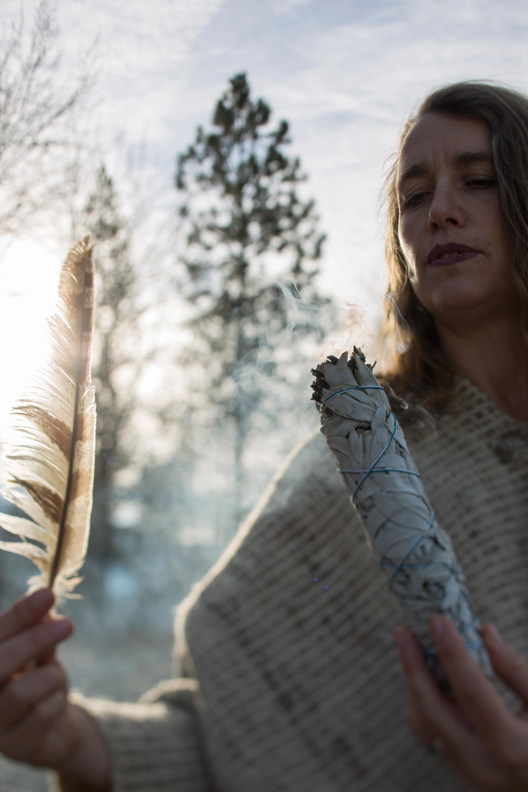 Woman holding sage bundle and feather during a cleansing ritual.