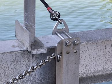 Close-up of a metal marine cleat with a chain and rope secured, near water.
