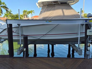 A boat lifted above water on a dock lift in a sunny marina.