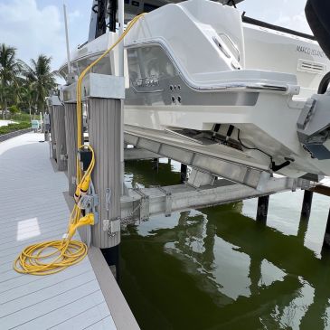 A boat lifted above the water on a dock lift system near palm trees.