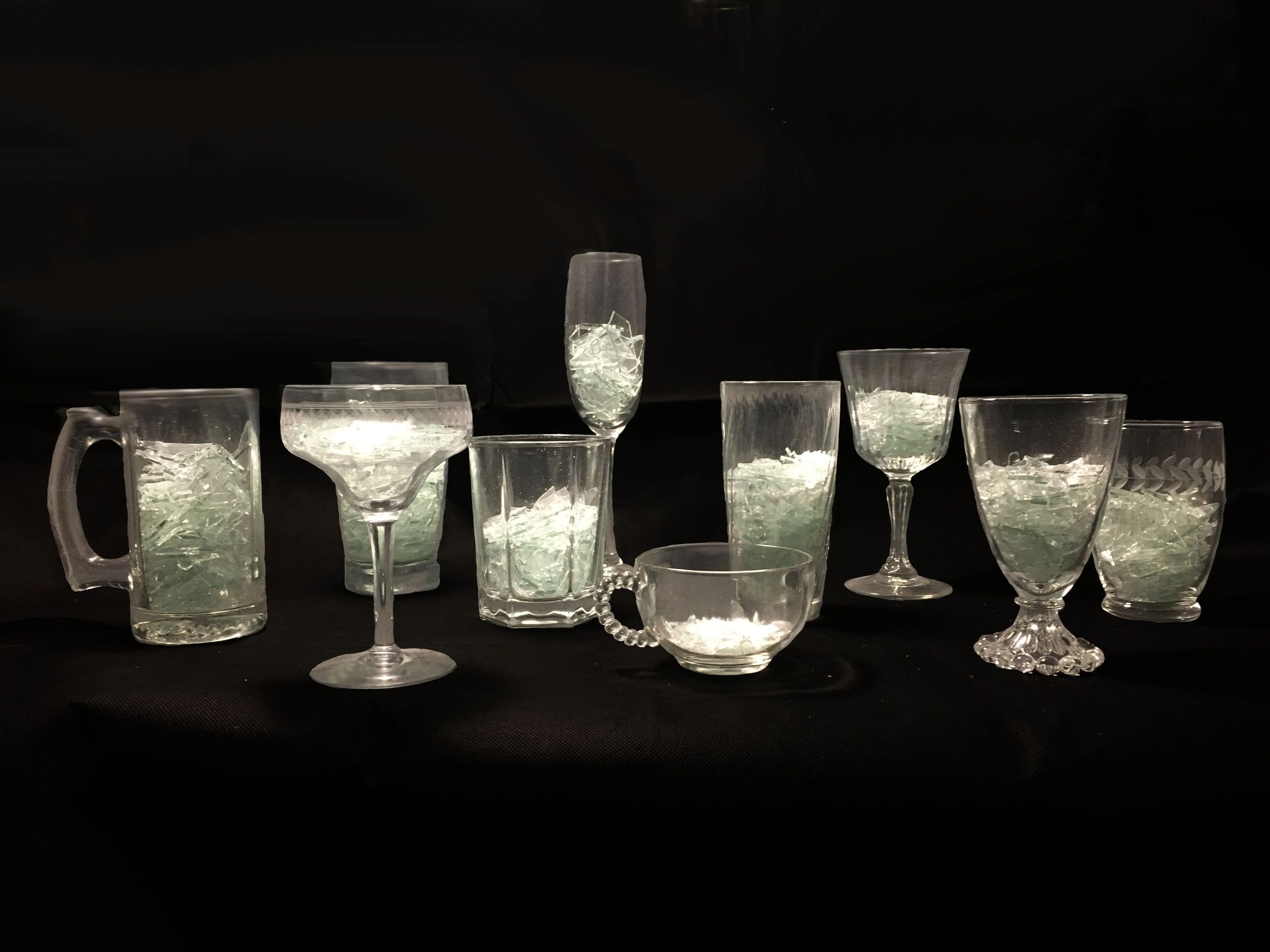 Photograph of several glasses full of broken glass with a black background