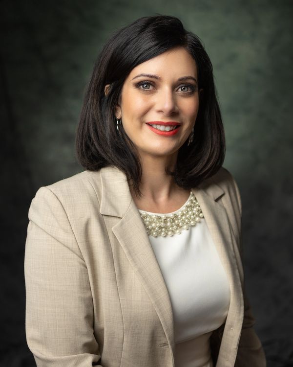 Professional woman in a beige blazer smiling warmly against a dark background.