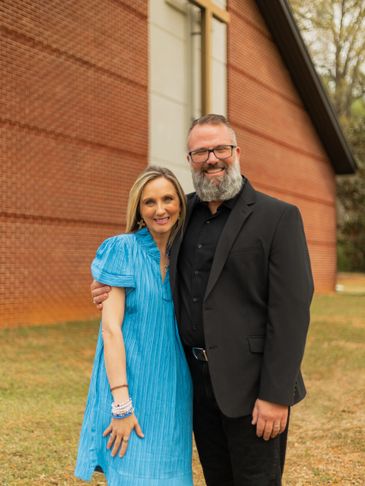 Couple posing happily outdoors near a brick building.