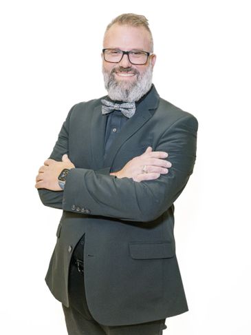 Smiling man with glasses and bow tie in a dark suit.