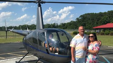 A couple stands next to a helicopter on a sunny day.