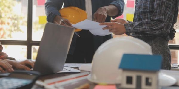 Construction professionals reviewing plans with a laptop and helmet on the table.