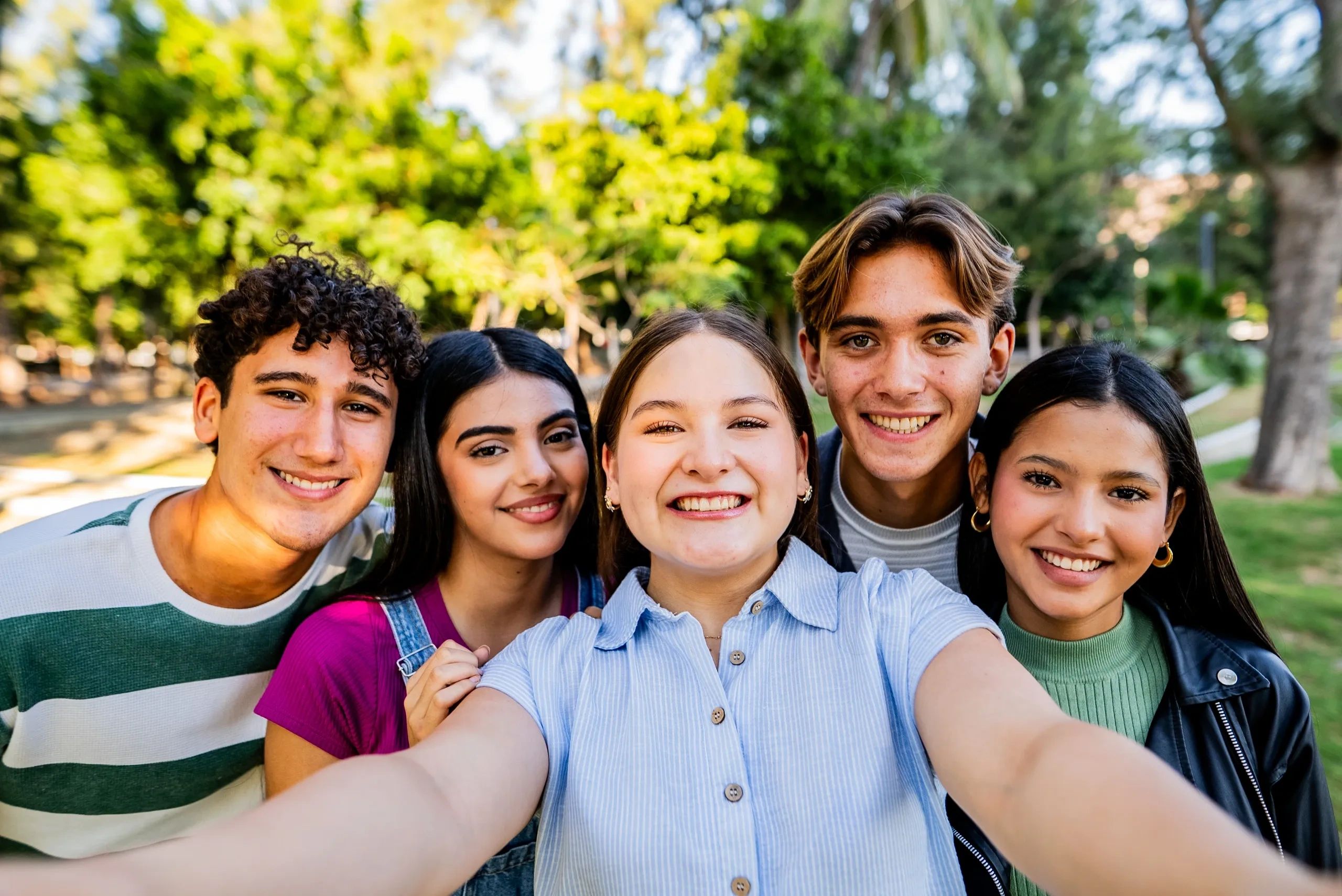 Group of five friends smiling for a selfie outdoors.