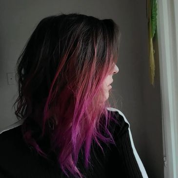 Woman with dark hair fading into bright pink, looking sideways.