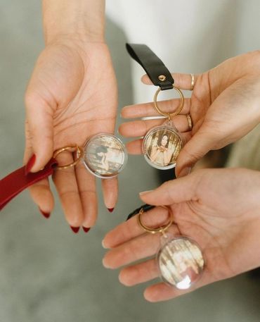 Three hands holding personalized photo keychains with leather straps.