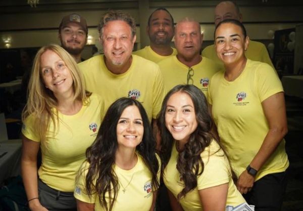 Group of smiling adults wearing matching yellow shirts.