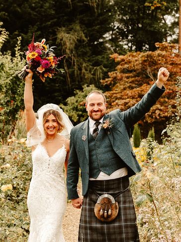 Bride holding her flowers and groom holding hands up in the air on their wedding day in St Andrews.
