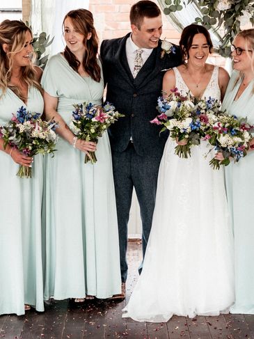 Group of bridesmaids and bride holding wildflower bouquets standing under an arch at a rustic barn.
