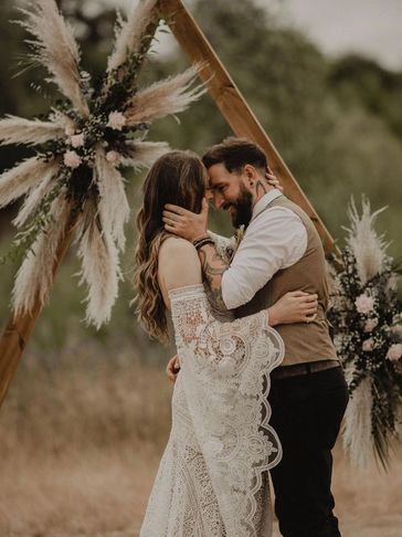 Bride and groom standing under a dried flower arch on a rustic barn. Outdoor ceremony.