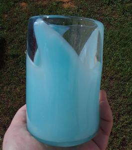 hand holding a glass cup with a solid color blue-green swirl design in front of a grass background.