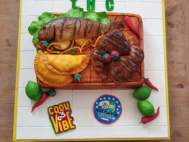 Cake decorated with grilled fish, steak, empanadas, and chili peppers.