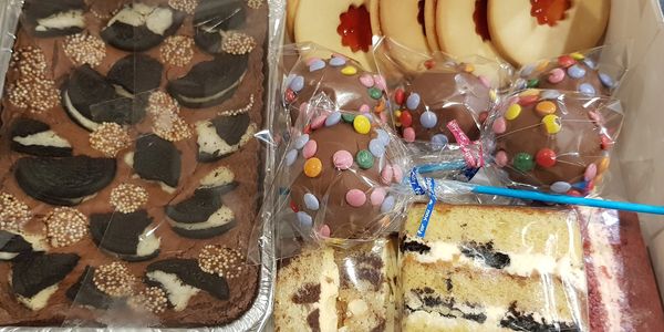 A box of assorted desserts including brownies, cookies, cake pops, and layered cakes.