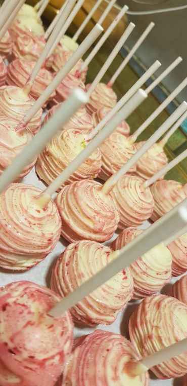 Rows of pink and white swirled cake pops with white sticks.