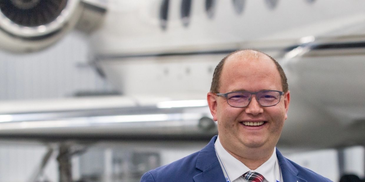 Smiling man in glasses and suit in front of an aircraft.