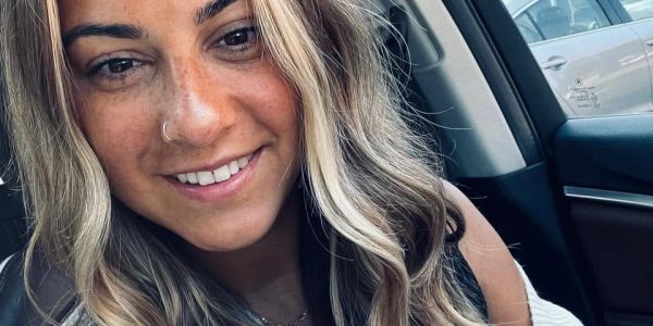 Smiling woman with long blonde hair inside a car.
