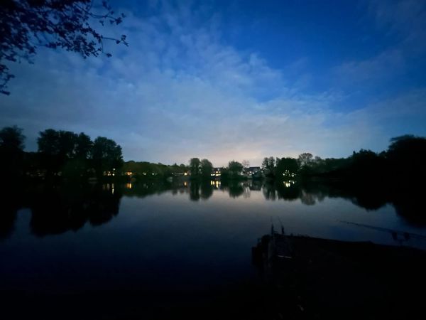 Calm lake at dusk with silhouetted trees and a blue sky.