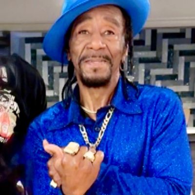 Man in bright blue outfit and hat posing with rings and chain.