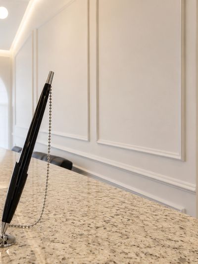 A black pen attached to a chain on a marble countertop in a minimalist room.