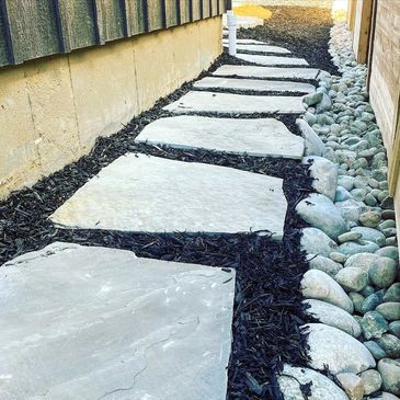 Stone pathway with black mulch and river rocks beside a house wall.