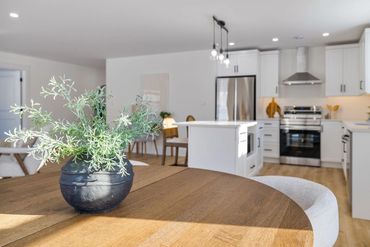 A modern kitchen with a wooden table and a plant centerpiece.