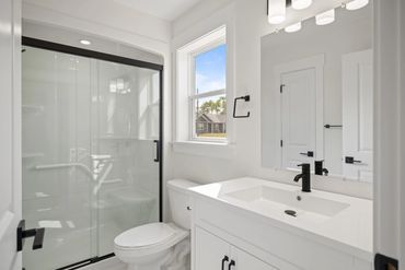 Modern white bathroom with black fixtures and glass shower doors.
