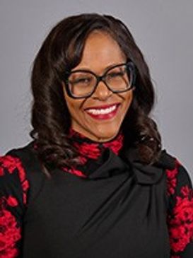 Smiling woman with glasses wearing a black and red floral dress.